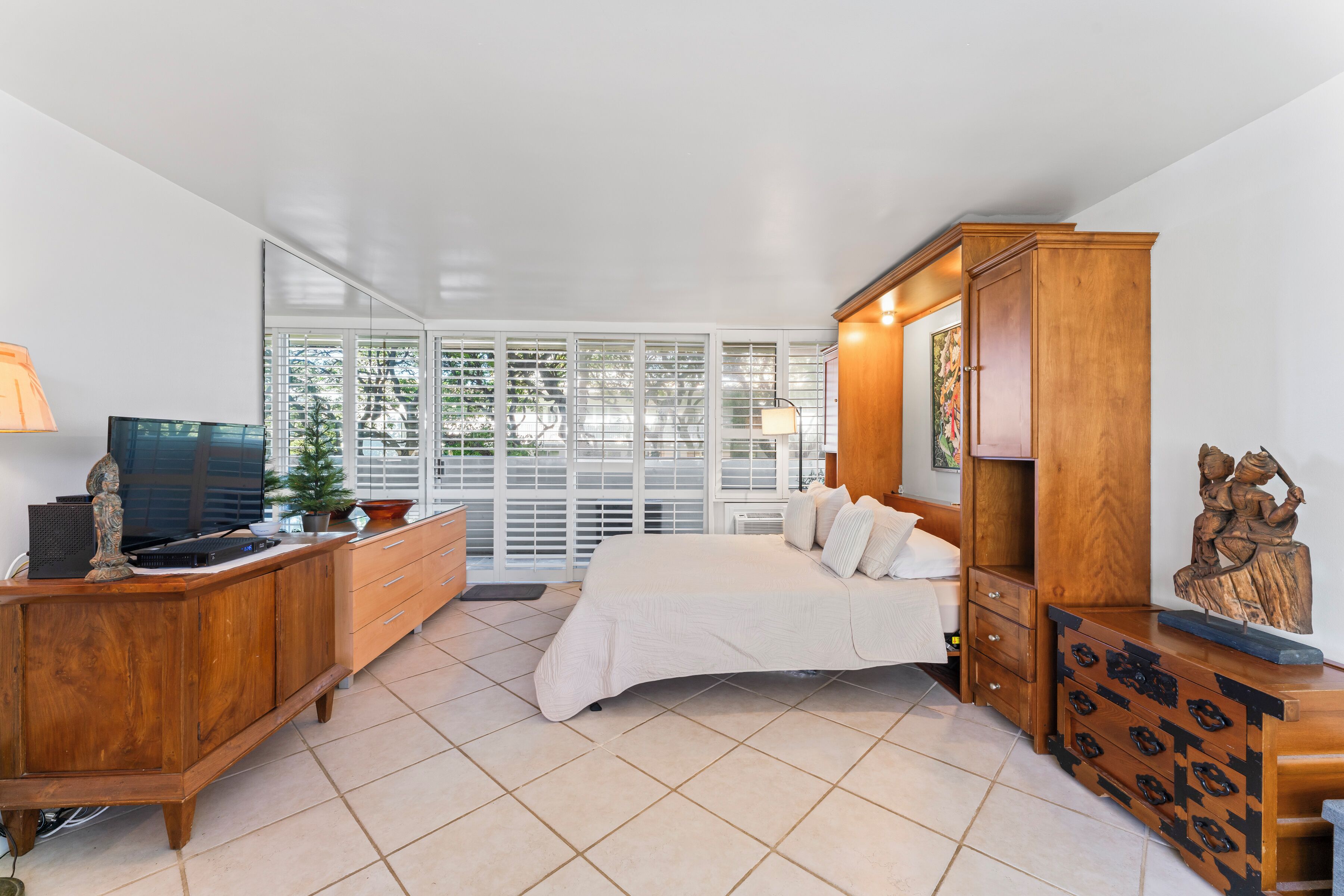 A bedroom with a bed, wooden furniture, a television, and large windows.