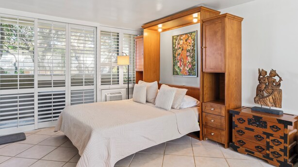 A bedroom with a large bed, wooden wardrobe, and a window with blinds. - Charming Studio Apartment with WiFi, AC in beautiful Diamond Head Beach Park! (Honolulu)