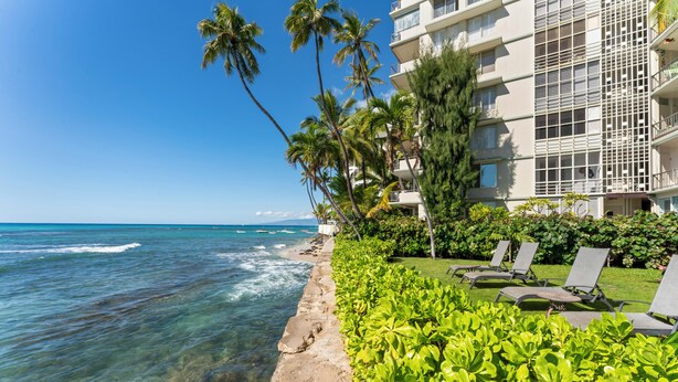 A beachfront hotel with a clear view of the ocean, palm trees, and lounge chairs.
