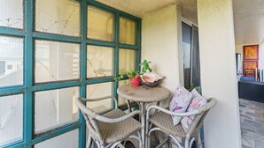 A corner room with a large window, wicker chairs, a small table with a plant, and a door. - Charming Studio Apartment with WiFi, AC in beautiful Diamond Head Beach Park! (Honolulu)