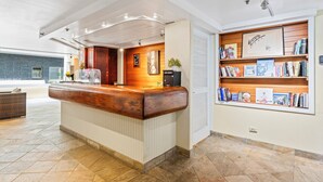 A reception area with a wooden reception desk, a wall-mounted bookshelf with books, and a large window with a view of the outside.