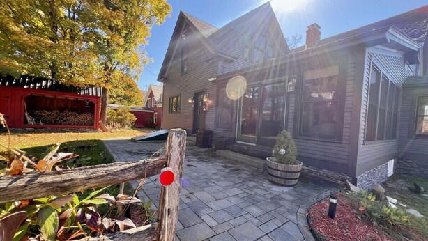 A wooden house with a porch, a red structure with a chimney, and a small tree in the yard.