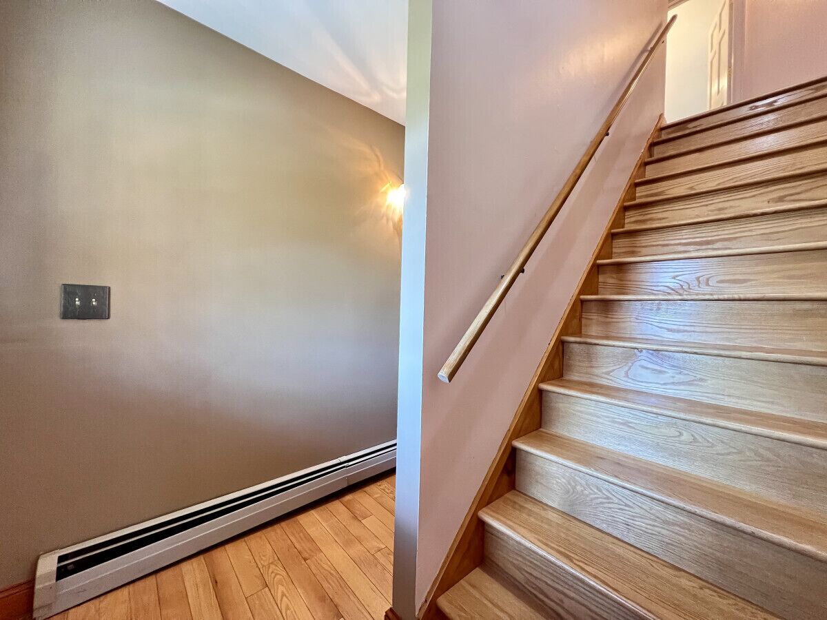 Un escalier avec des marches en bois et une rampe, un mur avec un interrupteur et un plancher doté d’un système de chauffage au sol.