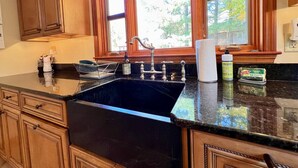 A kitchen with wooden cabinets, a black countertop, a stainless steel sink, and a window with a view of trees.