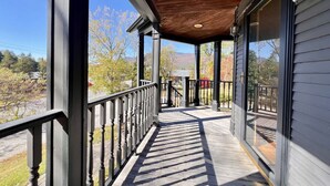 A covered porch with a wooden ceiling and metal railings, leading to a glass door.