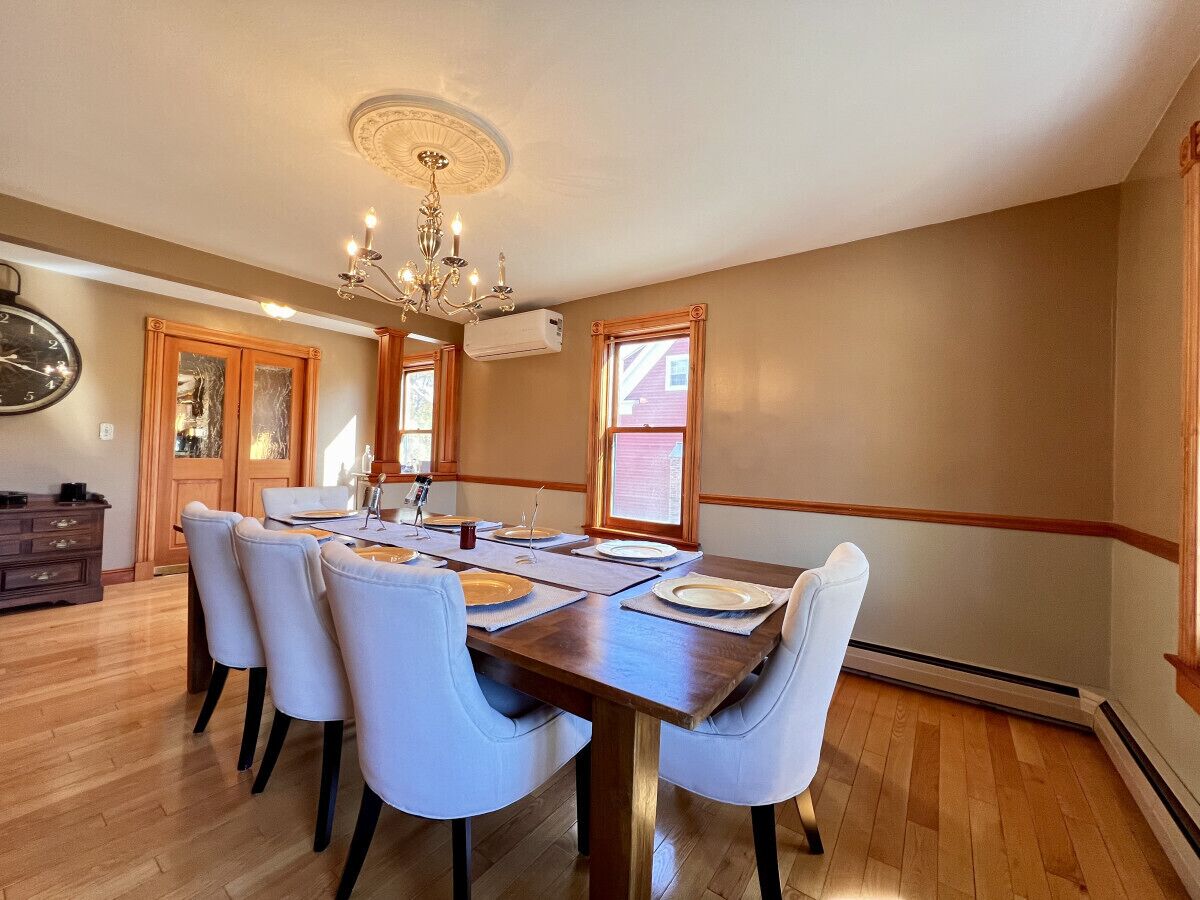 A dining room with a wooden table set for six, surrounded by six chairs.