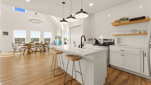Une cuisine moderne dotée d’un îlot central, de tabourets de bar, de luminaires suspendus et offrant une vue sur l’extérieur.