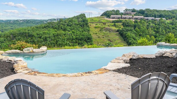 Une piscine bordée de pierres, entourée de chaises, avec en arrière-plan une végétation luxuriante et des bâtiments éloignés.