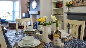 A dining table set with white plates, bowls, and wine glasses, a bottle of Trivento wine, and a vase with yellow and white flowers.