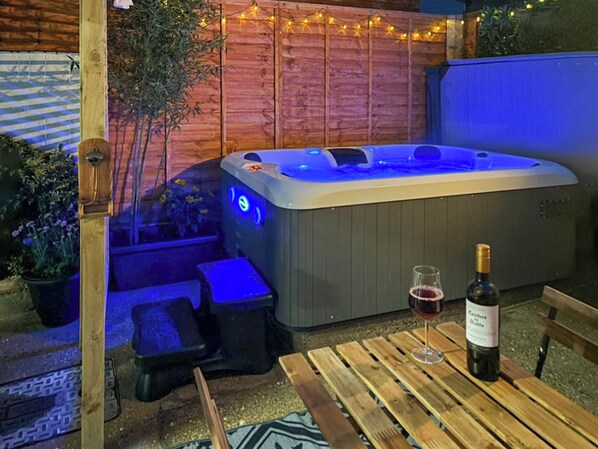 Un jacuzzi con cubierta de madera y una botella de vino sobre una mesa.