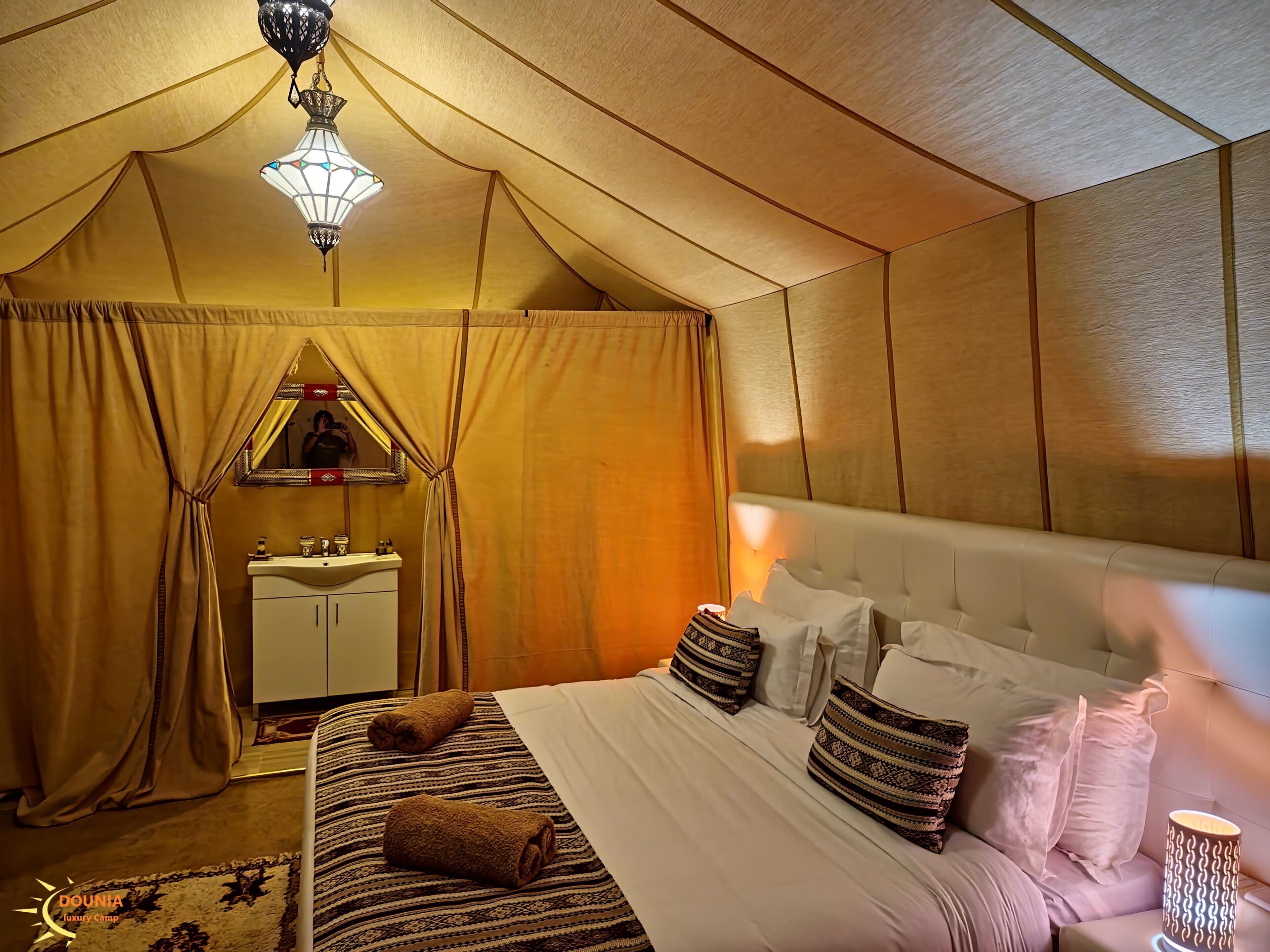 A tent-style room with a bed, a bedside lamp, and a mirror.