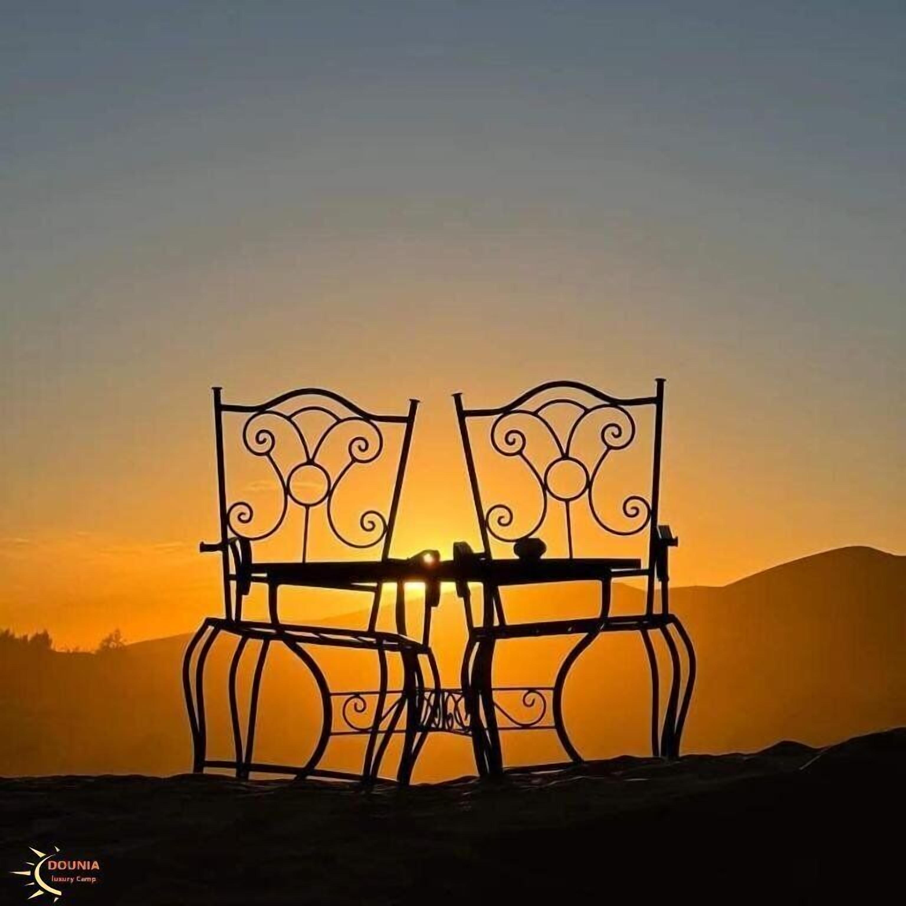 Two ornate metal chairs facing each other with a sunset in the background.