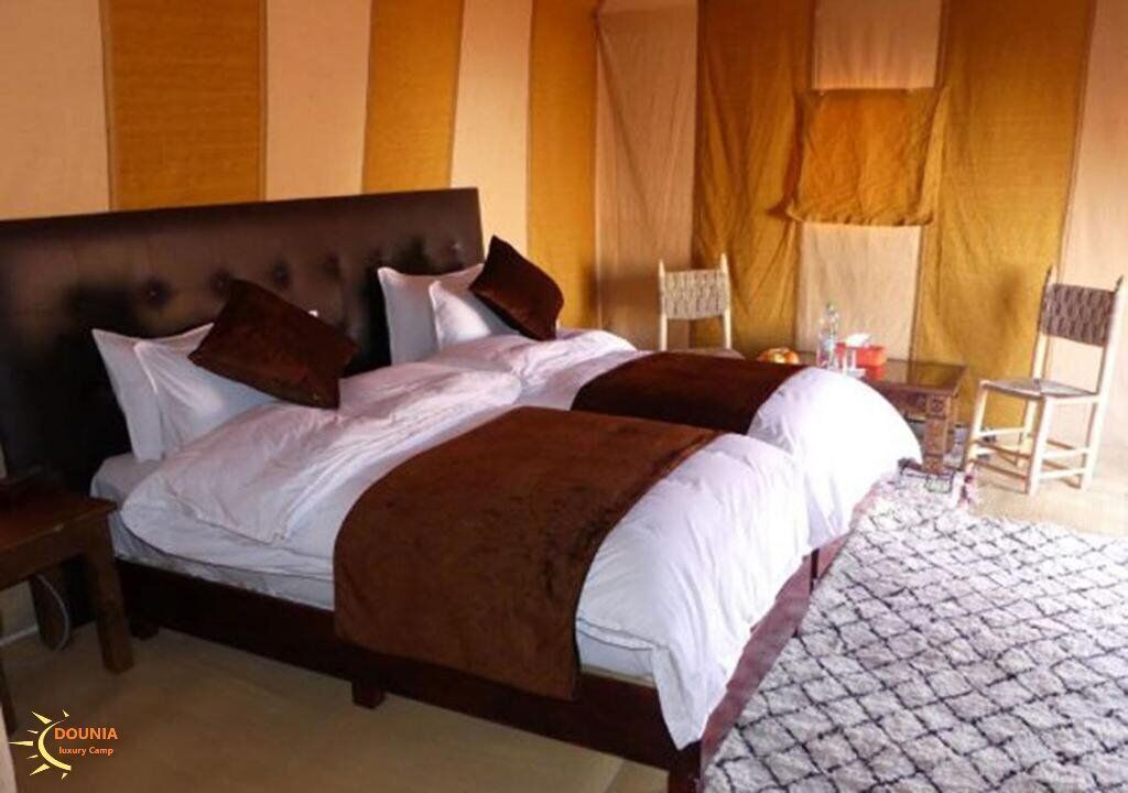 A double bed with a wooden headboard, two nightstands, a small table with a chair, and a patterned rug.