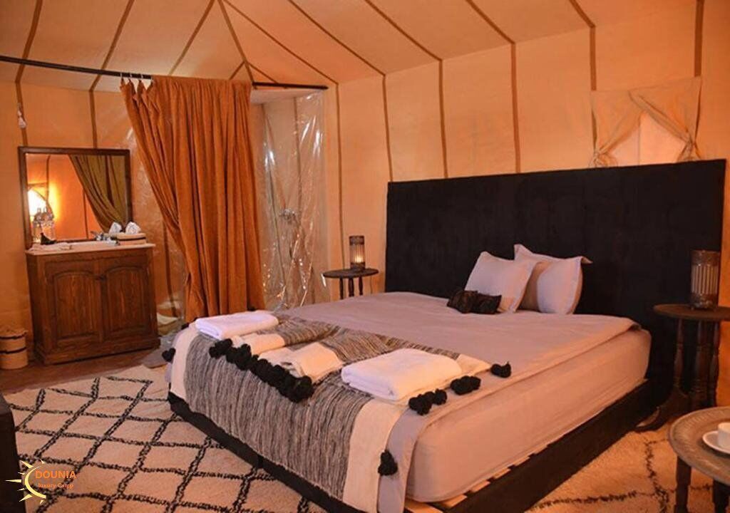 A tent-style bedroom with a large bed, a wooden dresser, and a small table.