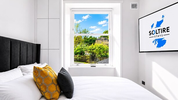 Een slaapkamer met een bed, een raam met uitzicht op groen en een bordje aan de muur.