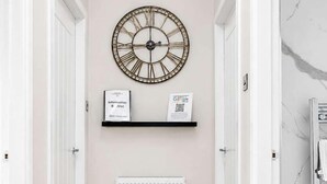 Een gang met een houten vloer, een witte radiator, een klok aan de muur en een deur aan de rechterkant.