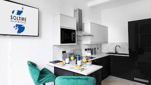 Een moderne keuken met een magnetron, kookplaat en spoelbak. Er staan twee groene stoelen en een ontbijtje klaar op het aanrecht.