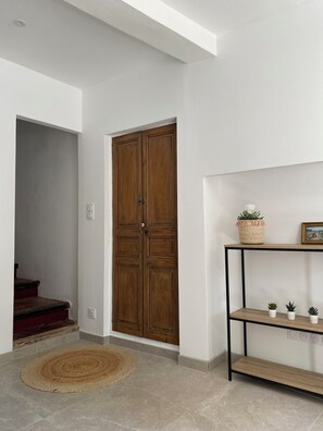 Enter through the classic wooden door into a serene space with a minimalist shelving unit and warm, textured rug.