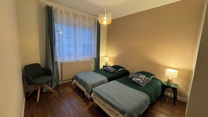 A bedroom with two beds, a chair, a window with curtains, and a hanging light fixture. - Cosy house Sables d'Olonne, 4 pers, town center (LES SABLES D'OLONNE)