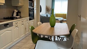 A modern kitchen with white cabinets, a dining table with chairs, and a green vase centerpiece. - Cosy house Sables d'Olonne, 4 pers, town center (LES SABLES D'OLONNE)