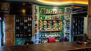 A bar with shelves of liquor bottles, a wooden counter, and a red chair. - De Rain Eco Beach Resort (Entebbe)