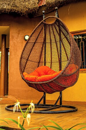 A wicker hanging chair with an orange cushion in front of a building with a thatched roof.