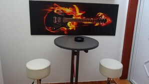 Une pièce dans laquelle on trouve un tableau représentant une guitare, accroché au mur, une petite table ronde sur laquelle est posé un objet noir, et deux tabourets blancs.