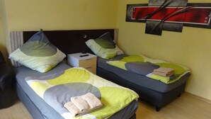 Une chambre avec deux lits, chacun doté d’une tête de lit, d’oreillers et d’une couverture. Il y a une table de chevet sur laquelle se trouve une télécommande.