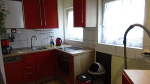 Une cuisine de taille réduite avec des meubles de rangement rouges, un évier, une cuisinière et une fenêtre.