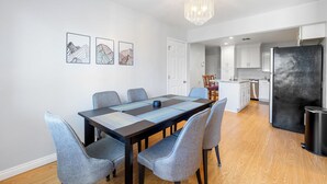 Une cuisine moderne avec des meubles blancs, un réfrigérateur noir et un coin repas comprenant une table et des chaises.