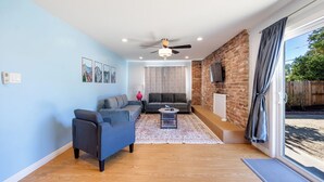 Un salon moderne avec un mur bleu, un ventilateur de plafond, une cheminée et une grande fenêtre avec des rideaux.