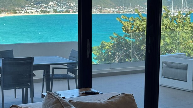 Un balcon avec un canapé et des fauteuils, donnant sur une plage et la mer.