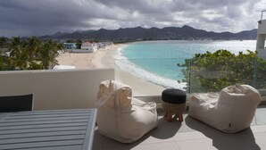 Un balcon avec deux fauteuils en forme de sac de haricots, une table et une vue sur une plage et des montagnes.