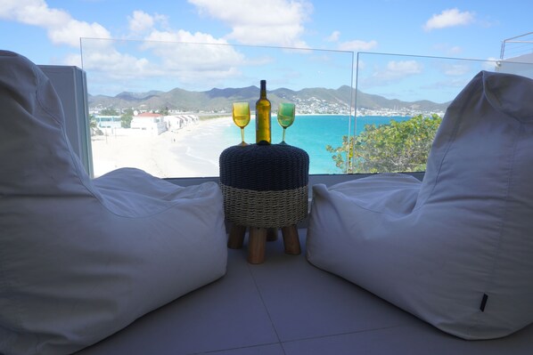 A balcony with white bean bag chairs, a wicker ottoman, and two wine glasses. - Luxury Penthouse with Private Rooftop Directly on Beach, Best Location, pool! (Simpson Bay)