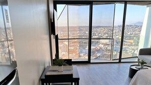 A modern apartment with a dining area, a bed, and a large window with a city view.