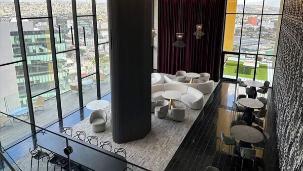 A modern lounge with a city view, featuring a large pillar, seating areas, and a glass railing.
