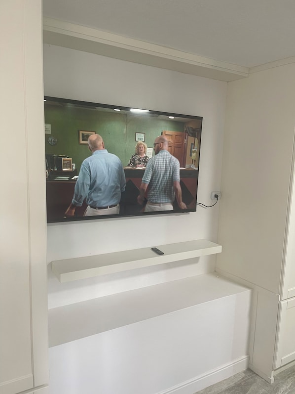 Ein Fernseher an einer weißen Wand, darunter ein Regal.