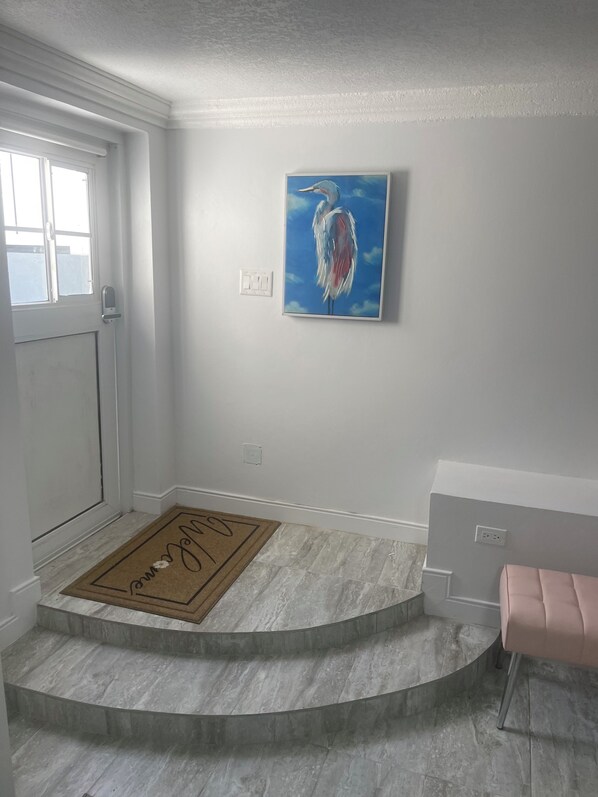 A clean, modern entryway with a marble floor, a doormat, a door, and a wall-mounted light switch.