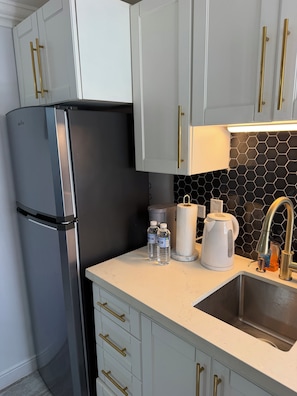 A modern kitchen with a stainless steel refrigerator, white cabinets with gold handles, a black hexagonal backsplash, and a stainless steel sink.