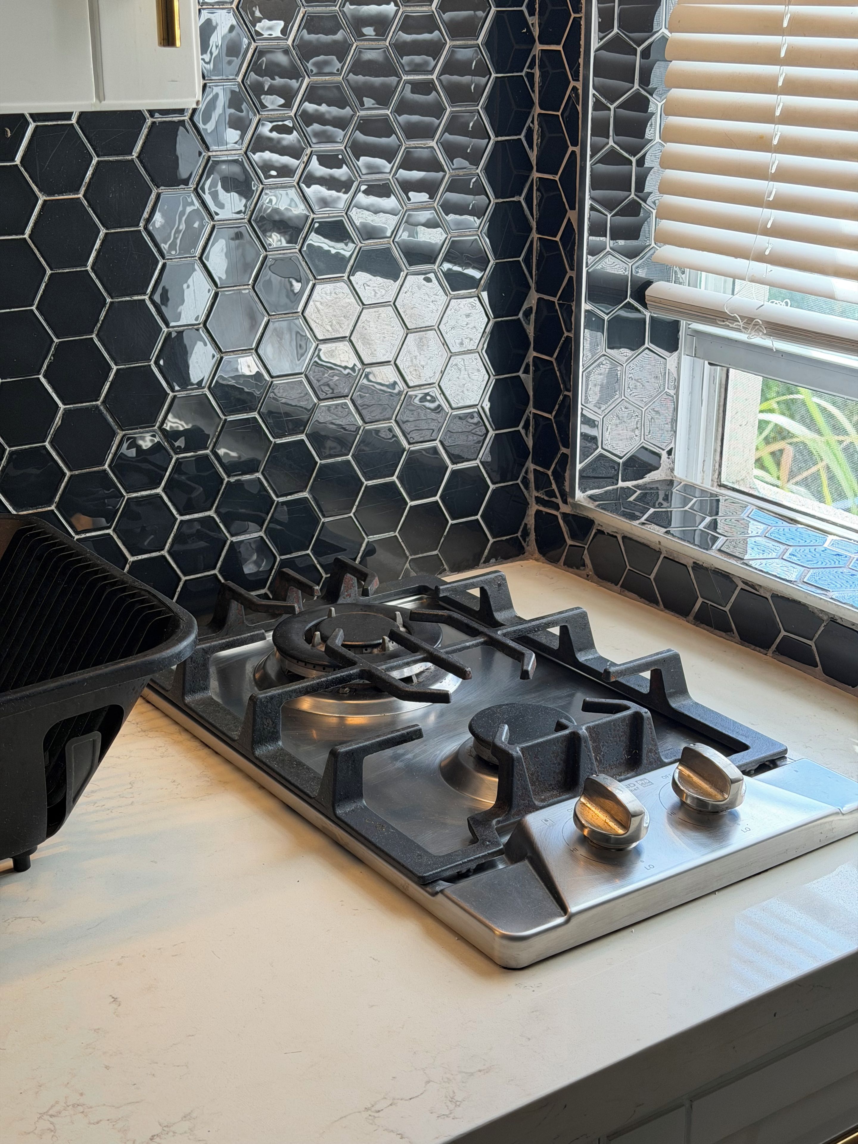 A kitchen with a gas stove, a hexagonal tile backsplash, and a window with blinds.