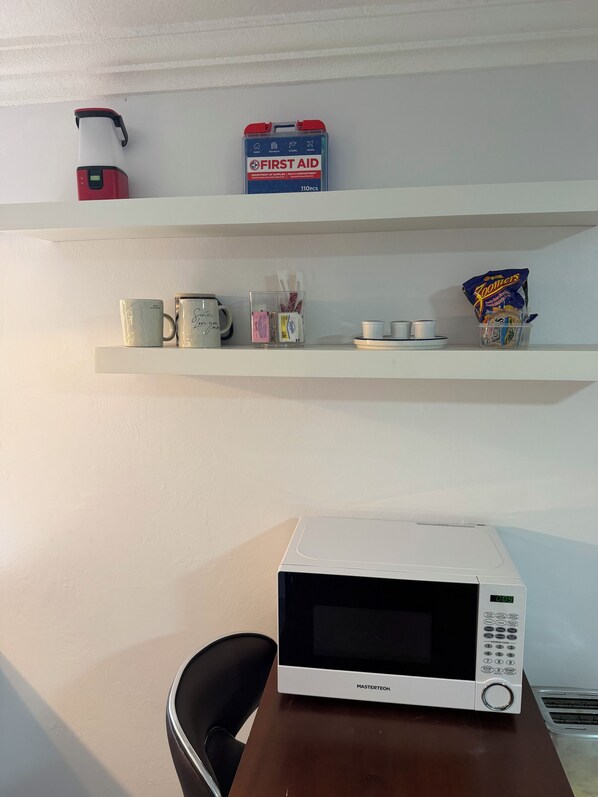 Un four à micro-ondes sur une table, une étagère avec une trousse de premiers secours et un paquet de chips.