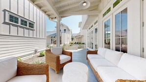 Eine überdachte Terrasse im Freien mit Korbmöbeln, einem weißen Sofa und einem runden Tisch.