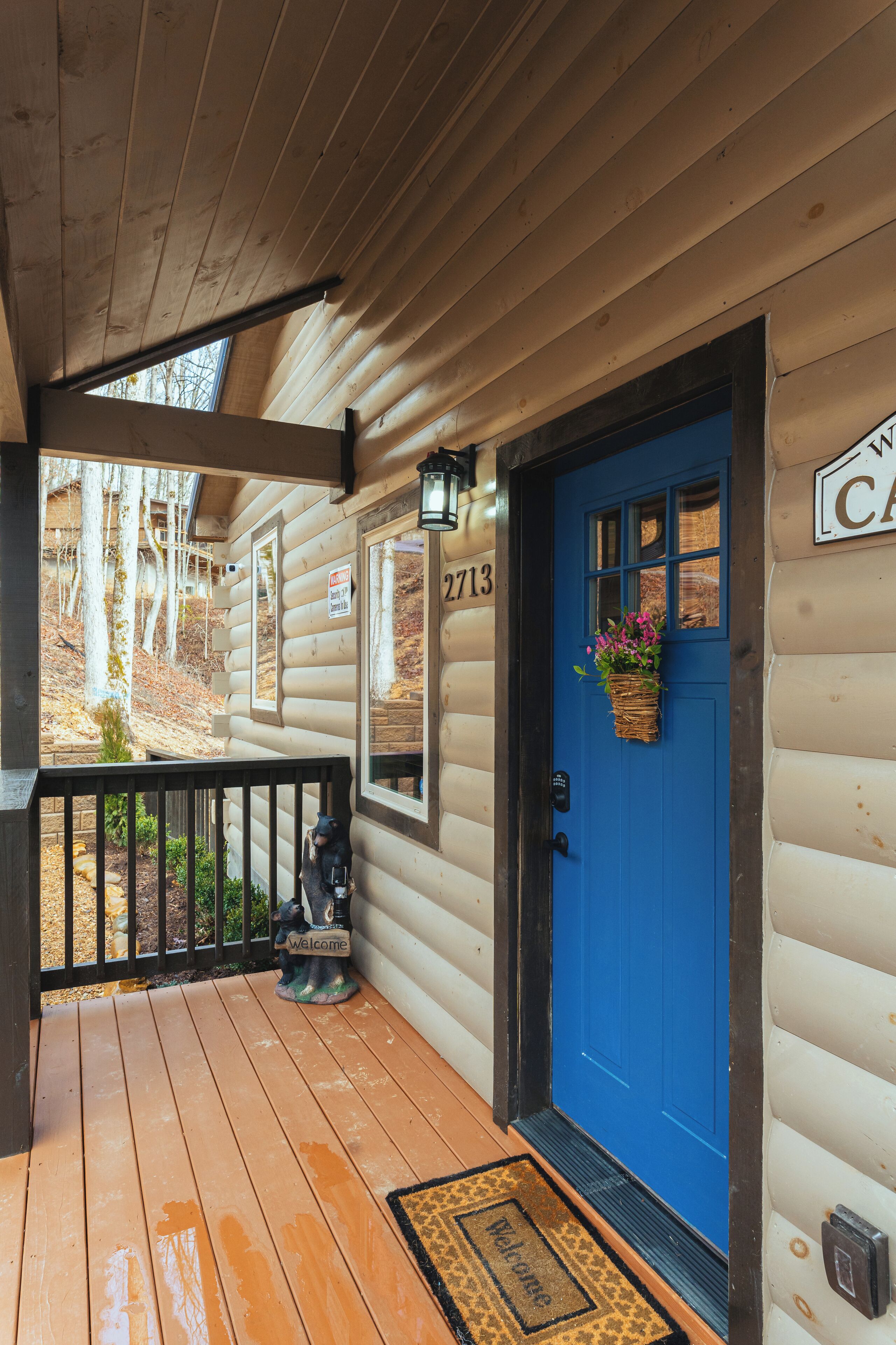 Une cabane en bois avec une porte bleue, une pancarte d’accueil et un panneau indiquant un numéro.
