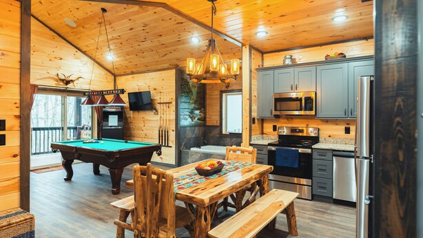 A wooden cabin interior with a pool table, wooden dining table, and a kitchen area. - New Build! Charming Wears Valley Cabin! Close to National Park and Attractions! (Sevierville)