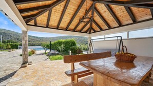 A covered outdoor seating area with a stone floor, wooden bench, and picnic table. - Lovely home in Cvrljevo with private swimming pool, can be inside or outside (Cvrljevo)