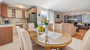 A modern kitchen with a dining area, featuring a round glass table, white chairs, and a view of the outdoors. - Lovely home in Cvrljevo with private swimming pool, can be inside or outside (Cvrljevo)