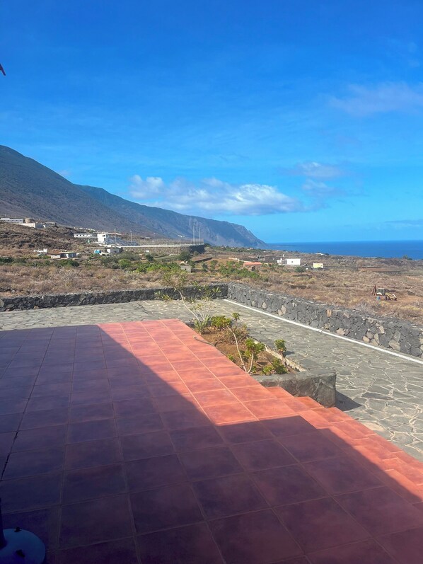 A coastal landscape with a paved area, stone walls, and buildings in the background.