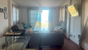 Una habitación moderna con una cama, un escritorio y una silla. Hay una ventana con cortinas, una lámpara colgante y un televisor en la pared.