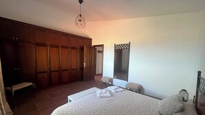 Un dormitorio con una cama grande, un armario, un banco y un espejo.