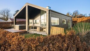 A modern house with a large glass front, a wooden deck, and a garden area. - 3 bedroom beautiful home in Nibe (Nibe)